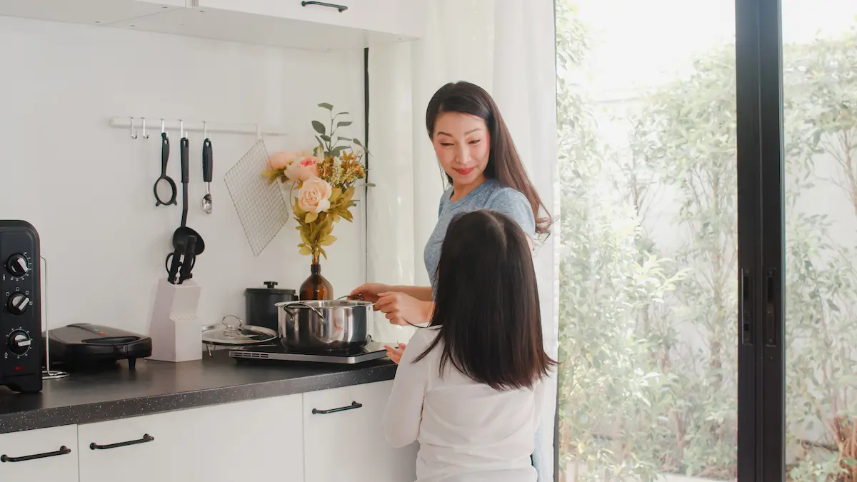 A child talking to her mom, who is cooking in the kitchen