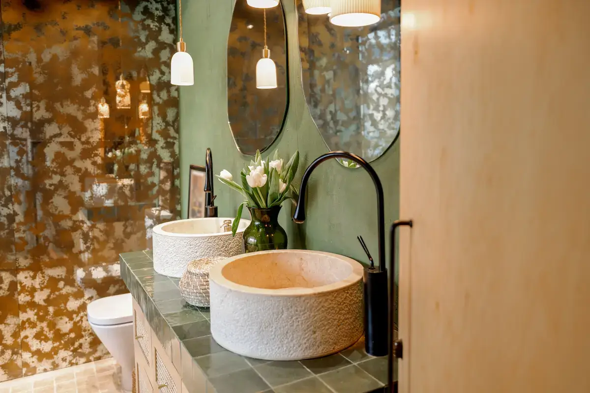 Modern bathroom design Singapore featuring double stone sinks, elegant pendant lighting, and contemporary green tile interiors.